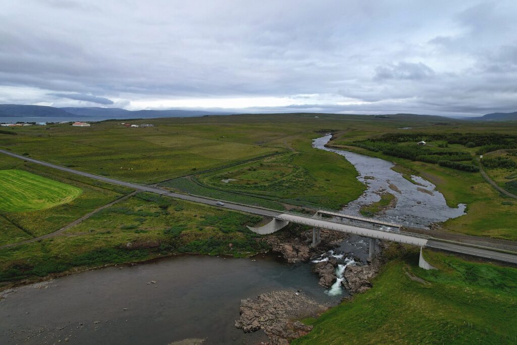 River valley and bridge with open pasture and distant farmhouses (Dalabyggð)