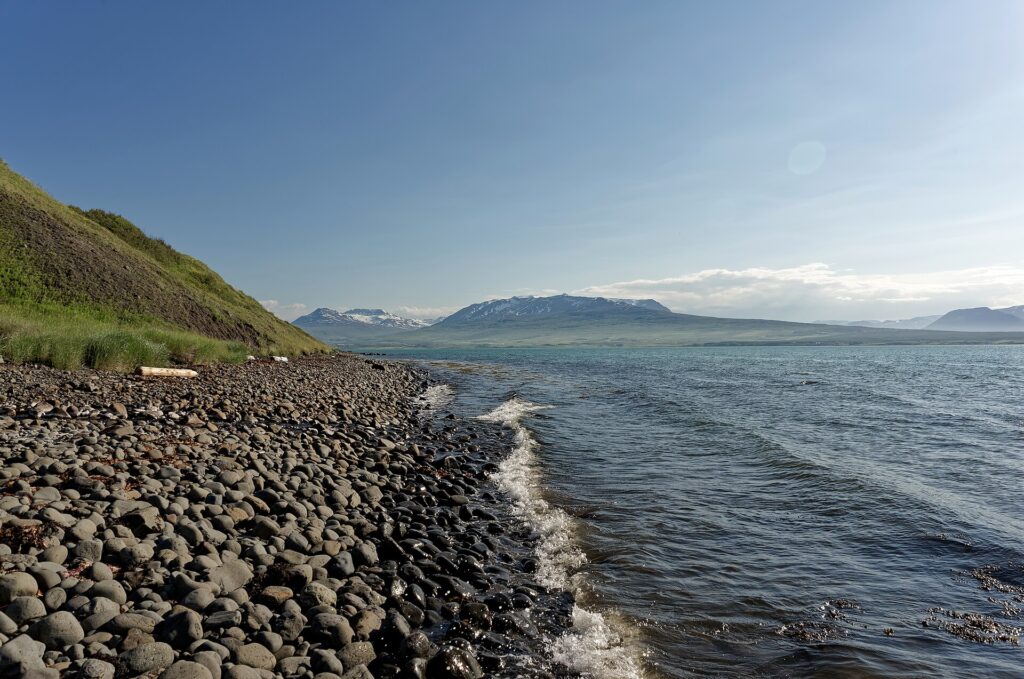 Pebble beach with waves lapping the shore and distant mountains (Svalbarðsstrandarhreppur)