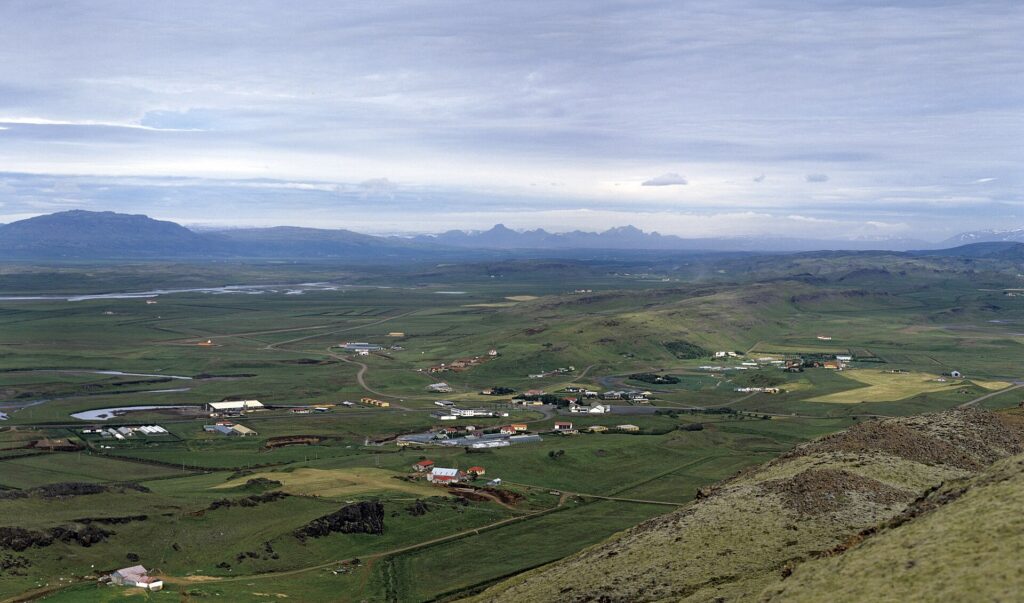 Wide view over farmland with greenhouses and rural buildings (Hrunamannahreppur)