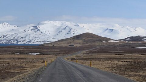 Road stretching toward a low hill with snow‑covered mountains beyond (Skagafjörður)