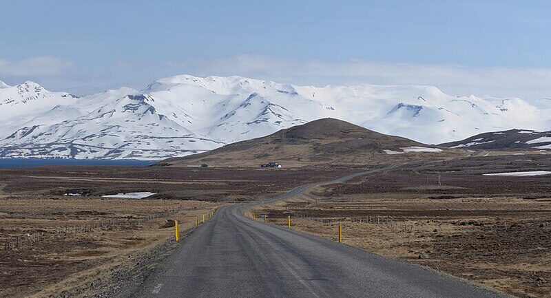 Road stretching toward a low hill with snow‑covered mountains beyond (Skagafjörður)