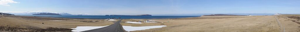 Panoramic fjord view with road leading to coastal buildings and distant islands (Skagafjörður)