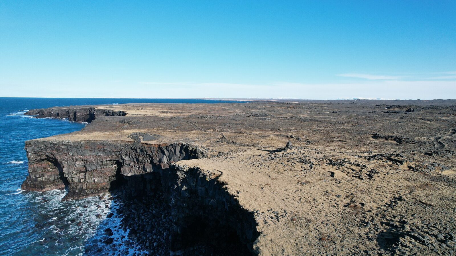 Rocky coastal cliffs with waves breaking at their base (Hafnir)