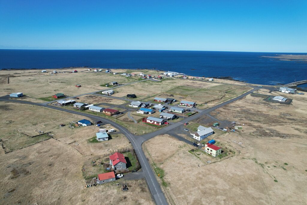 Aerial view of low houses, roads and shoreline with a small pier (Hafnir)