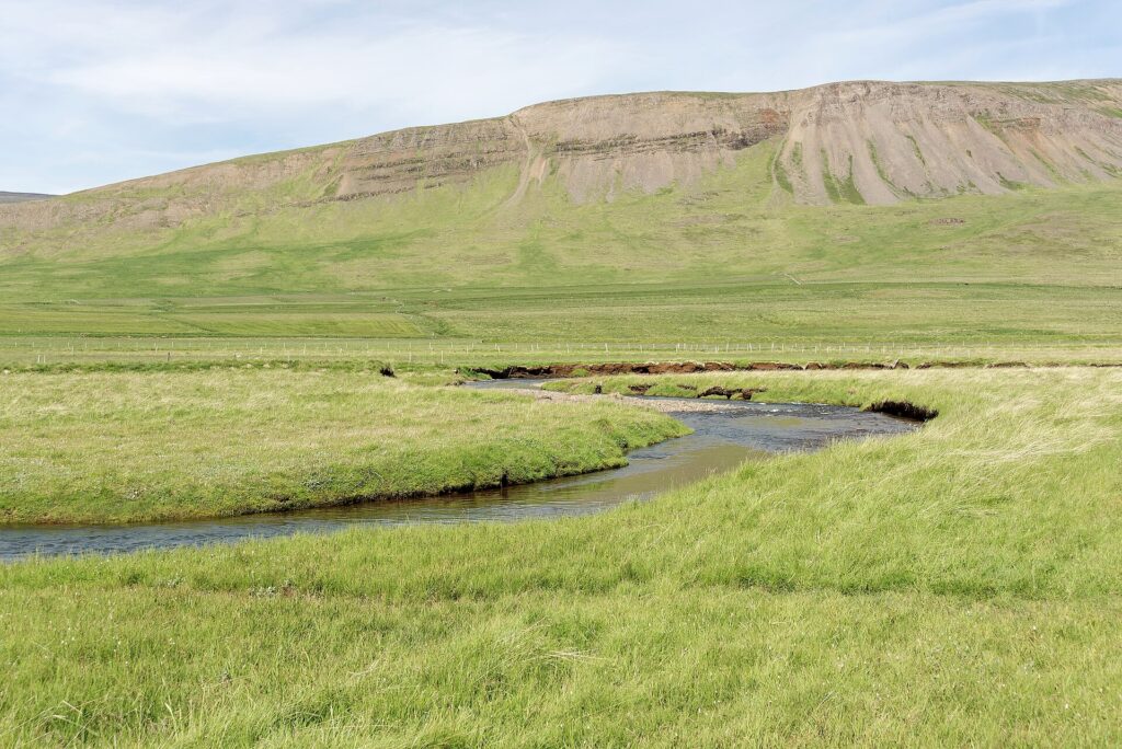 Meandering stream across grassy plains with steep hillside behind (Húnaþing vestra)
