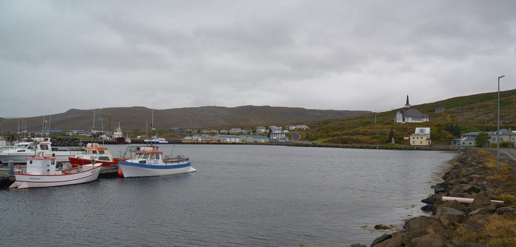 Harbour with fishing boats and a white church on the hillside (Hólmavík)