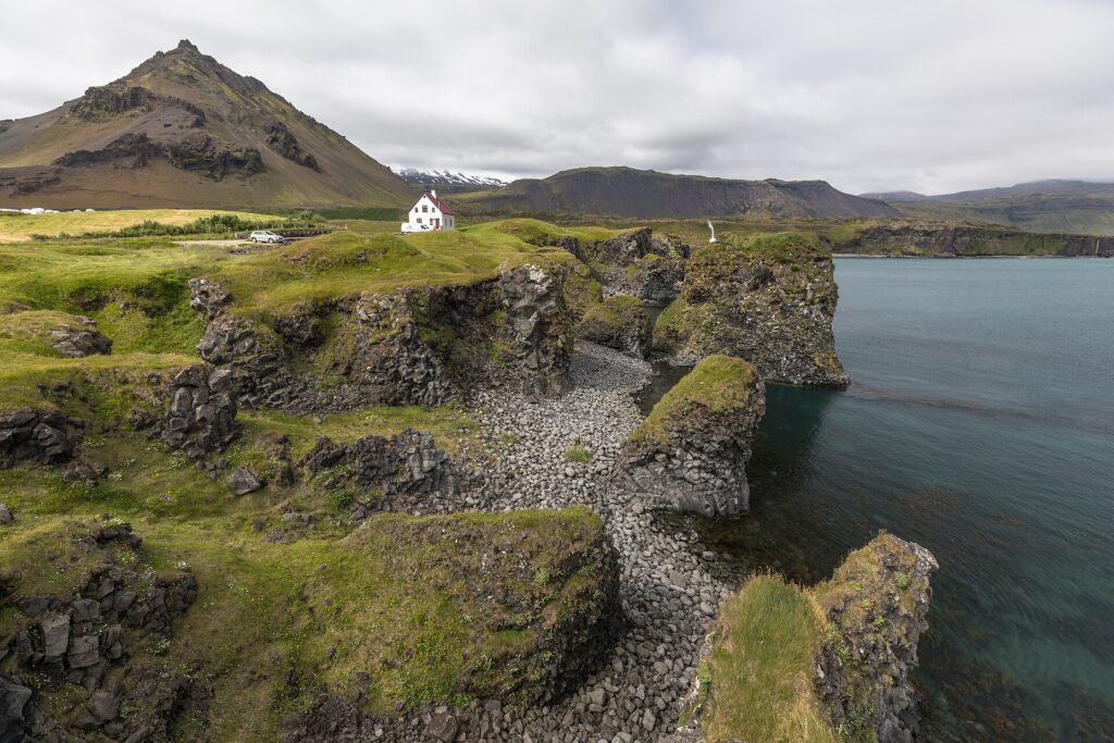White house on grassy headland above rocky cliffs and calm bay (Snæfellsbær)
