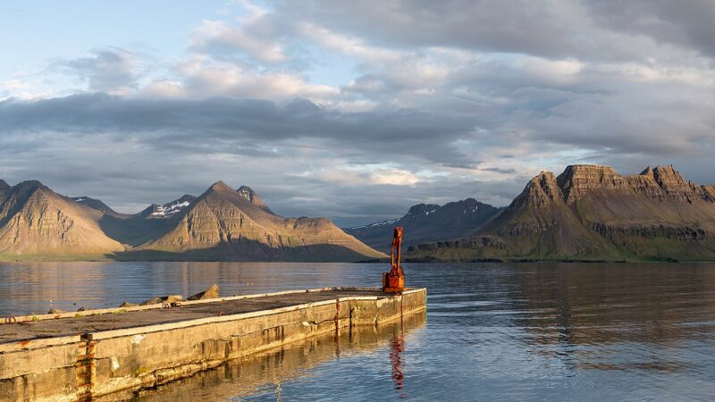 Concrete pier projecting into still water with mountains beyond (Árneshreppur)