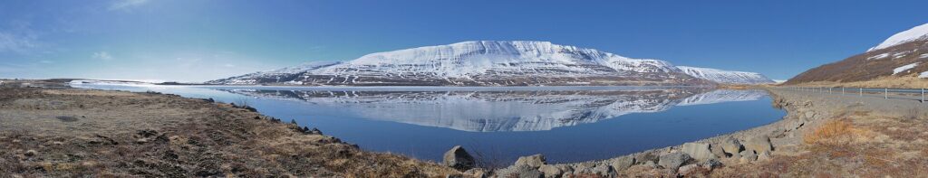 Snow-capped mountain reflected in a calm lake with rocky shore (Þingeyjarsveit)