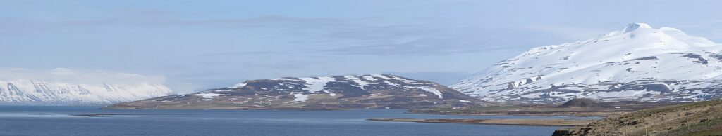 Snow-dusted hills and shoreline across a calm fjord (Grýtubakkahreppur)