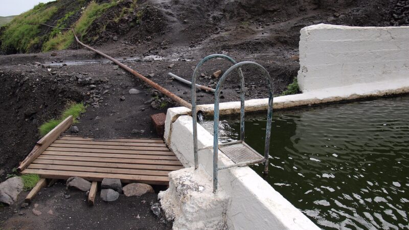 Pool ladder, concrete edge and long hot-water pipe on the hillside (Seljavallalaug)