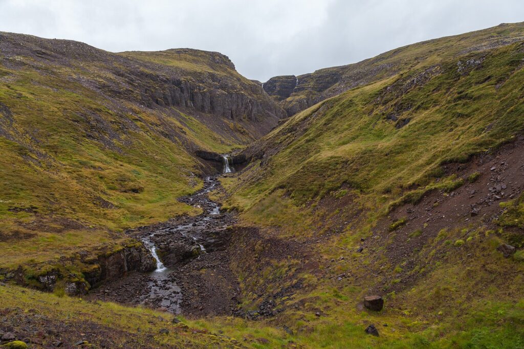 A narrow ravine with a small waterfall and steep grassy slopes (Borgarbyggð)