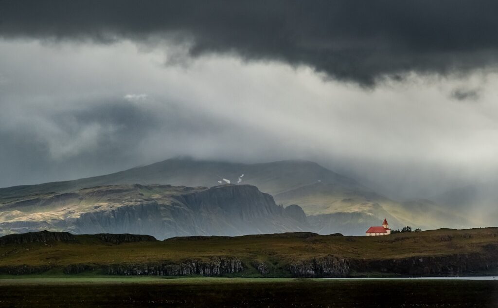 A solitary church beneath dramatic low clouds and distant mountains (Borgarbyggð)