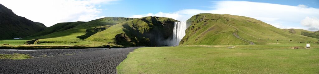 Wide view of waterfall with grassy foreground and hills (Skógafoss)