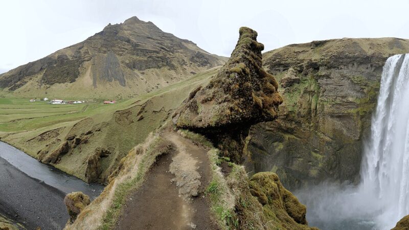 Waterfall beside river with farmland and cliffs (Skógafoss)