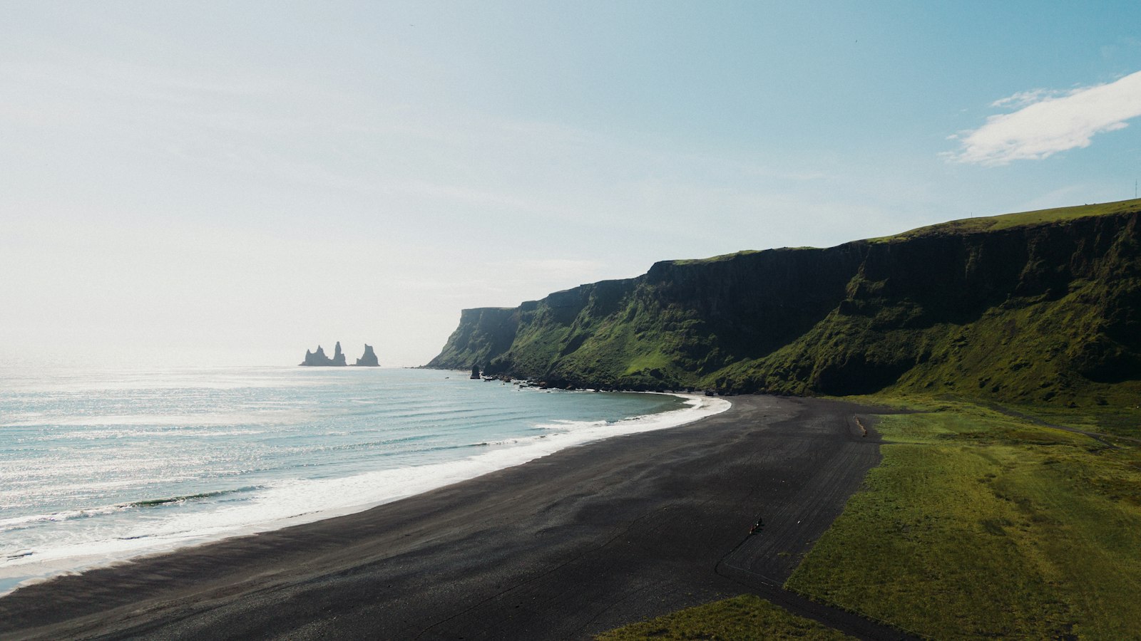 Black sand beach below green cliffs with sea stacks