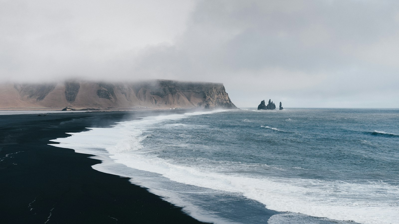 Waves on a black sand beach below cliffs at Vík